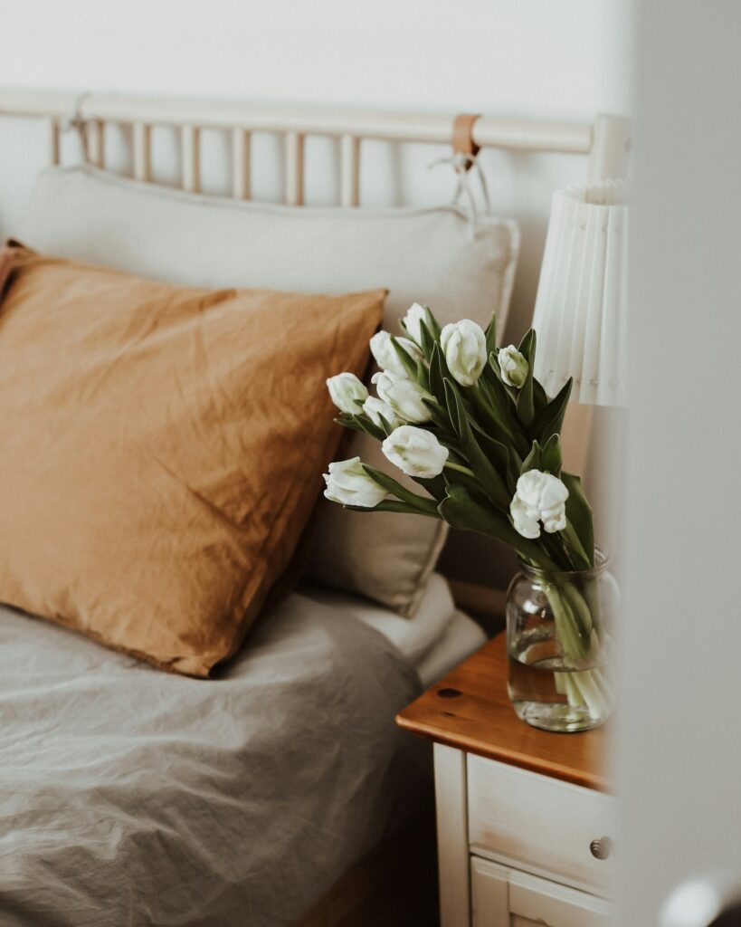 cozy bed with beside table storage with white tulips in a vase