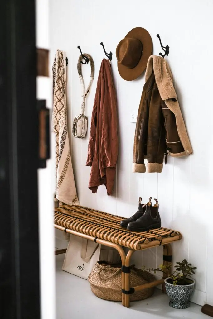 Stylish entryway decor with coats, hat, and boots on rattan bench.