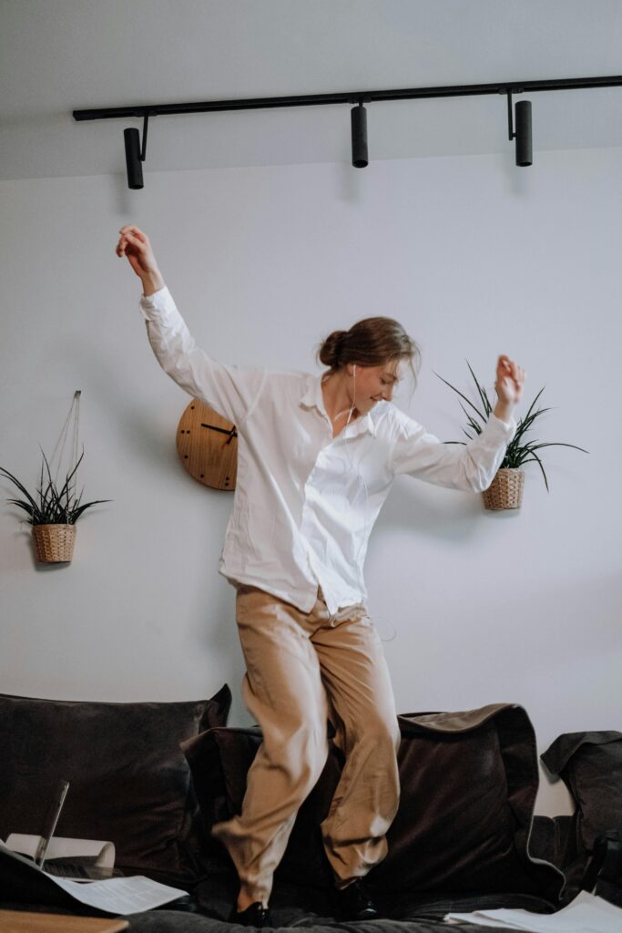 A woman joyfully dances in her living room, enjoying music and expressing freedom.